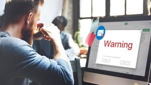 Man drinking coffee with email warning popping on computer screen
