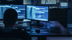 Man on multiple computers in dark room 